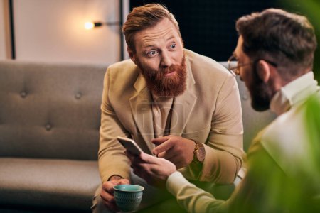 Photo for Handsome bearded man talking to his interviewer in glasses that holding smartphone during discussion - Royalty Free Image