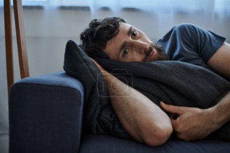 hombre barbudo deprimido en traje casual acostado en el sofá durante la ruptura, conciencia de la salud mental