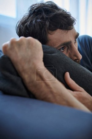 Foto de Frustrado hombre barbudo en ropa casera casual acostado en el sofá durante la ruptura, conciencia de salud mental - Imagen libre de derechos