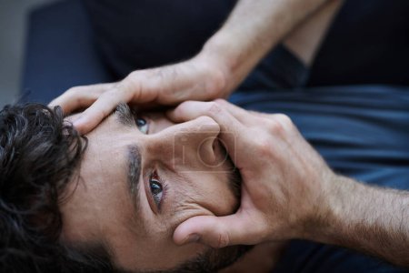 stressed desperate man with beard in casual attire lying with hands on face during mental breakdown