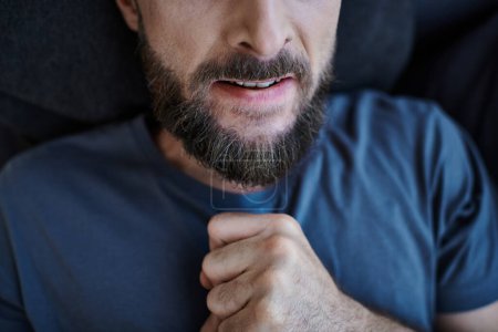 Ausgeschnittene Ansicht eines bärtigen gestressten Mannes in Alltagskleidung, der während eines Nervenzusammenbruchs auf dem Sofa liegt