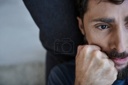 gestresster verzweifelter Mann mit Bart in Freizeitkleidung, der mit den Händen vor dem Gesicht während eines Nervenzusammenbruchs liegt