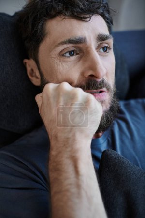 Téléchargez les photos : Homme désespéré stressé avec la barbe en tenue décontractée couché avec les mains sur le visage pendant la dépression mentale - en image libre de droit