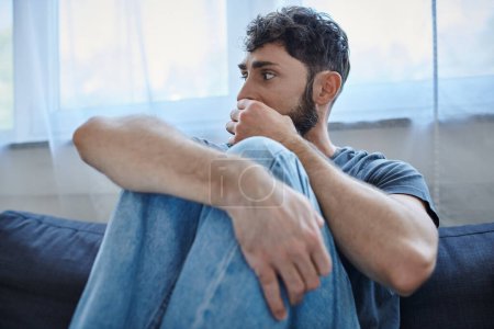 Traumatisierter ängstlicher Mann in Freizeitkleidung sitzt bei Zusammenbruch auf Sofa, Bewusstsein für psychische Gesundheit