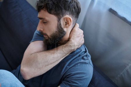 ängstlicher verzweifelter Mann in Hauskleidung, der während einer depressiven Episode auf dem Sofa liegt, Bewusstsein für psychische Gesundheit