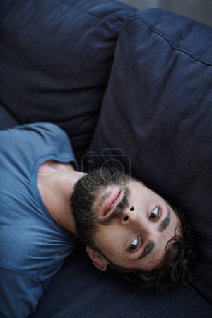 Foto de Desesperado hombre deprimido en camiseta casual acostado en el sofá durante el episodio depresivo, salud mental - Imagen libre de derechos