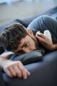 traumatized suffering man with beard lying on sofa with pills in hand, mental health awareness Poster #694538172