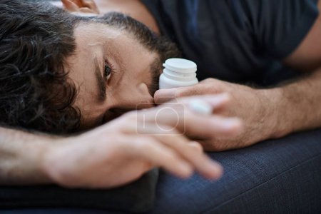 Foto de Hombre ansioso deprimido en traje casual acostado en el sofá con pastillas en la mano, conciencia de la salud mental - Imagen libre de derechos