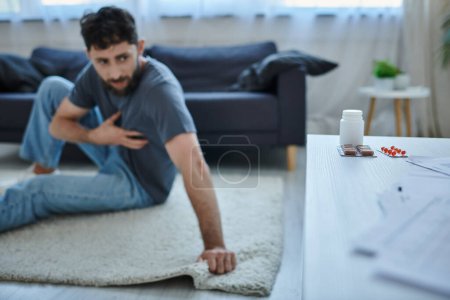 Photo for Focus on pills on table with blurred anxious man with depressive episode on backdrop, mental health - Royalty Free Image