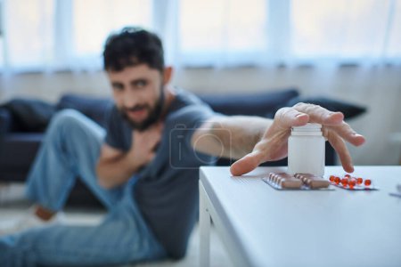 Konzentration auf Tabletten auf dem Tisch mit verschwommenem ängstlichen Mann mit depressiver Episode auf dem Hintergrund, psychische Gesundheit