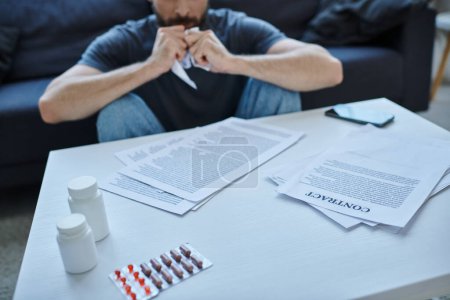 Foto de Vista recortada del hombre enfermo sentado en la mesa con papeles y pastillas en él durante la crisis mental - Imagen libre de derechos