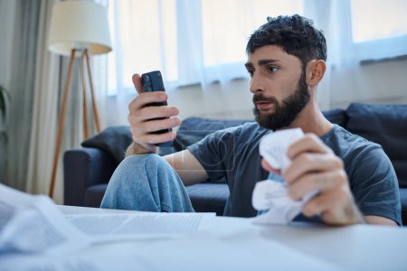 Foto de Deprimido hombre que sufre mirando a su teléfono inteligente durante el episodio depresivo, salud mental - Imagen libre de derechos