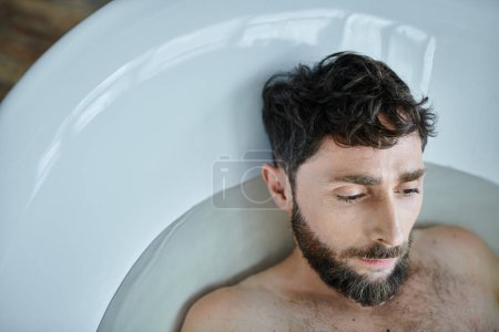 hombre frustrado deprimido con barba acostado en la bañera durante la ruptura, conciencia de salud mental