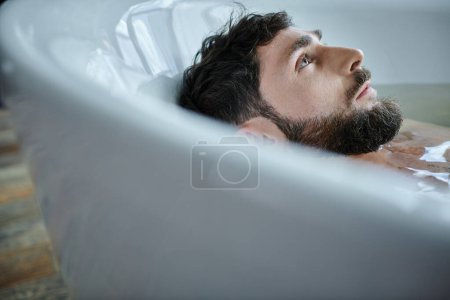 Foto de Hombre frustrado deprimido con barba acostado en la bañera durante la ruptura, conciencia de salud mental - Imagen libre de derechos