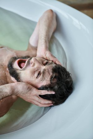 Photo for Emotional traumatized man lying in bathtub  and screaming during breakdown, mental health awareness - Royalty Free Image
