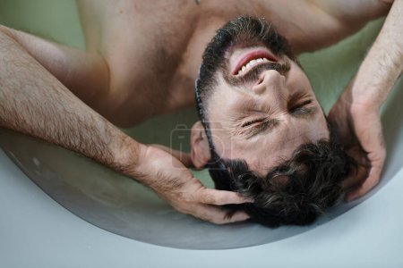 Foto de Angustioso hombre traumatizado acostado en la bañera y llorando durante el colapso, conciencia de salud mental - Imagen libre de derechos