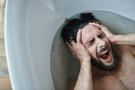 Foto de Hombre traumatizado emocional acostado en la bañera y gritando durante la ruptura, conciencia de salud mental - Imagen libre de derechos