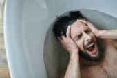 emotional traumatized man lying in bathtub  and screaming during breakdown, mental health awareness Poster #694539520