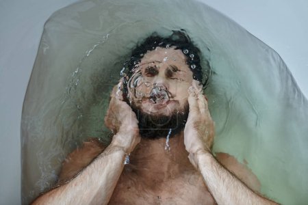 Téléchargez les photos : Frustré homme déprimé avec barbe noyée dans la baignoire pendant la panne, conscience de la santé mentale - en image libre de droit