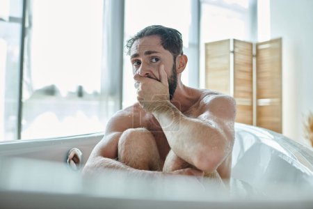 Foto de Hombre ansioso sentado en la bañera con las manos cerca de la cara durante el colapso, conciencia de salud mental - Imagen libre de derechos