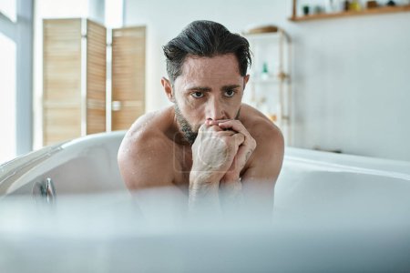 Foto de Hombre ansioso sentado en la bañera con las manos cerca de la cara durante el colapso, conciencia de salud mental - Imagen libre de derechos