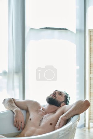 Foto de Hombre frustrado traumatizado con barba acostado en la bañera durante la ruptura, conciencia de salud mental - Imagen libre de derechos