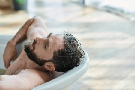 Traumatisierter frustrierter Mann mit Bart liegt bei Zusammenbruch in Badewanne