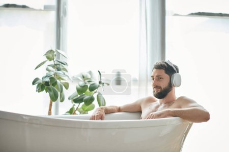 jolly good looking man with beard and headphones sitting and relaxing in his bathtub, mental health