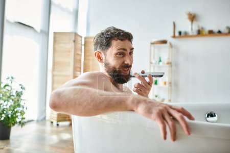 jolly handsome man with beard lying in bathtub and recording audio message, mental health awareness