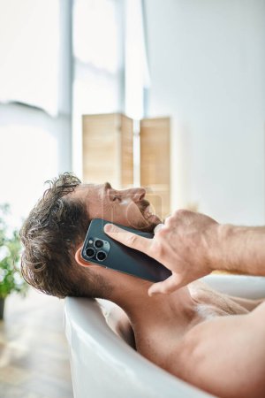 jolly attractive man with beard lying in bathtub and talking by phone, mental health awareness