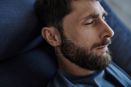 depressed anxious man with beard in casual attire lying on sofa during mental breakdown, awareness
