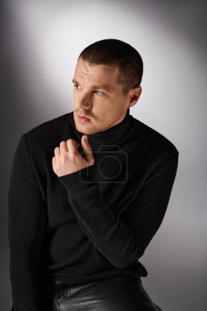 thoughtful handsome stylish man in black turtleneck looking away on grey backdrop with lighting