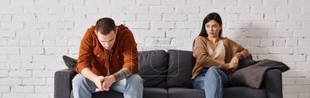 joven pareja interracial ofendido sentado en el sofá en la sala de estar, concepto de divorcio familiar, pancarta