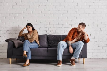 Photo for Depressed multiethnic couple sitting on couch in living room at home, family divorce concept - Royalty Free Image