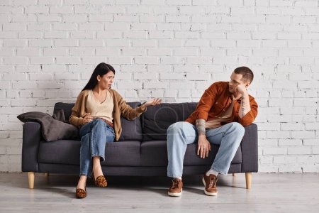 displeased interracial couple sitting on couch in living room at home, family divorce concept