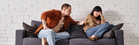 Téléchargez les photos : Mari irrité parler à jeune asiatique femme pleurer sur canapé dans salon, bannière horizontale - en image libre de droit