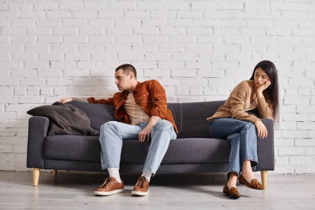 Téléchargez les photos : Jeune couple interracial avec détresse émotionnelle assis sur le canapé dans le salon, concept de divorce - en image libre de droit
