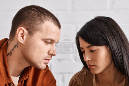 young and upset interracial couple talking in living room at home at home, relationship difficulties
