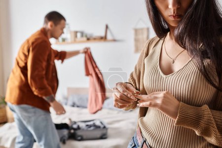 abgeschnittene Ansicht einer jungen Frau, die ihren Ehering in der Nähe des Mannes ablegt, der Koffer packt, Scheidung der Familie