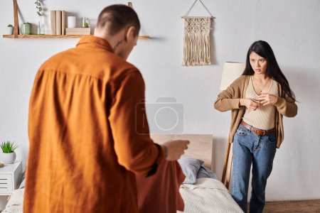 beleidigte Asiatin zieht Ehering aus, Mann steht mit Kleidung im Schlafzimmer, Scheidung
