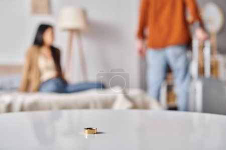 selektiver Fokus des Eherings auf dem Tisch in der Nähe eines gemischtrassigen Paares, das sich im Schlafzimmer streitet, Scheidung