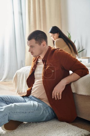 Photo for Young  offended man sitting on floor near upset asian wife, relationship difficulties concept - Royalty Free Image