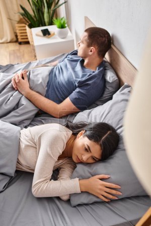 Téléchargez les photos : Vue grand angle de jeune et bouleversé couple interracial couché sur le lit à la maison, problèmes familiaux - en image libre de droit