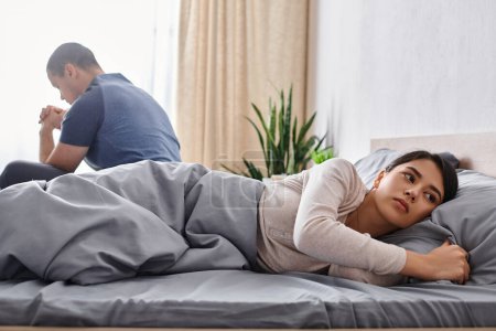 Téléchargez les photos : Bouleversé asiatique femme regardant loin près mari assis sur lit à la maison, relations difficultés - en image libre de droit
