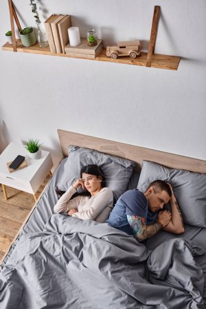 Téléchargez les photos : Vue grand angle de couple multiculturel frustré couché sur le lit à la maison, problèmes familiaux - en image libre de droit