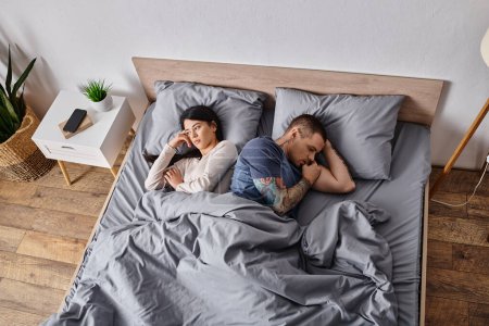 high angle view of upset multiethnic couple lying down on bed at home, family divorce concept