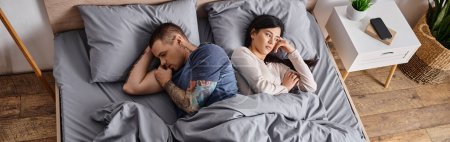 Téléchargez les photos : Vue grand angle de jeune couple multiethnique triste couché sur le lit à la maison, bannière horizontale - en image libre de droit