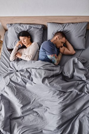 high angle view of depressed interracial couple lying down on bed at home, family divorce concept
