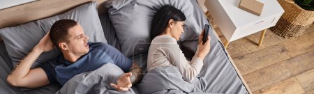 irritated man quarreling at young asian wife looking in his smartphone in bedroom, banner