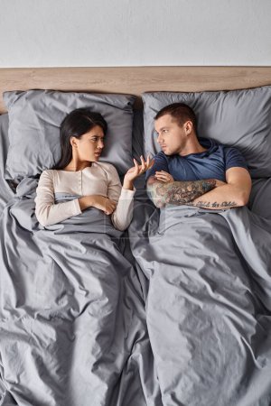 Téléchargez les photos : Vue de dessus de jeune couple interracial couché avec les bras croisés et se quereller sur le lit à la maison - en image libre de droit